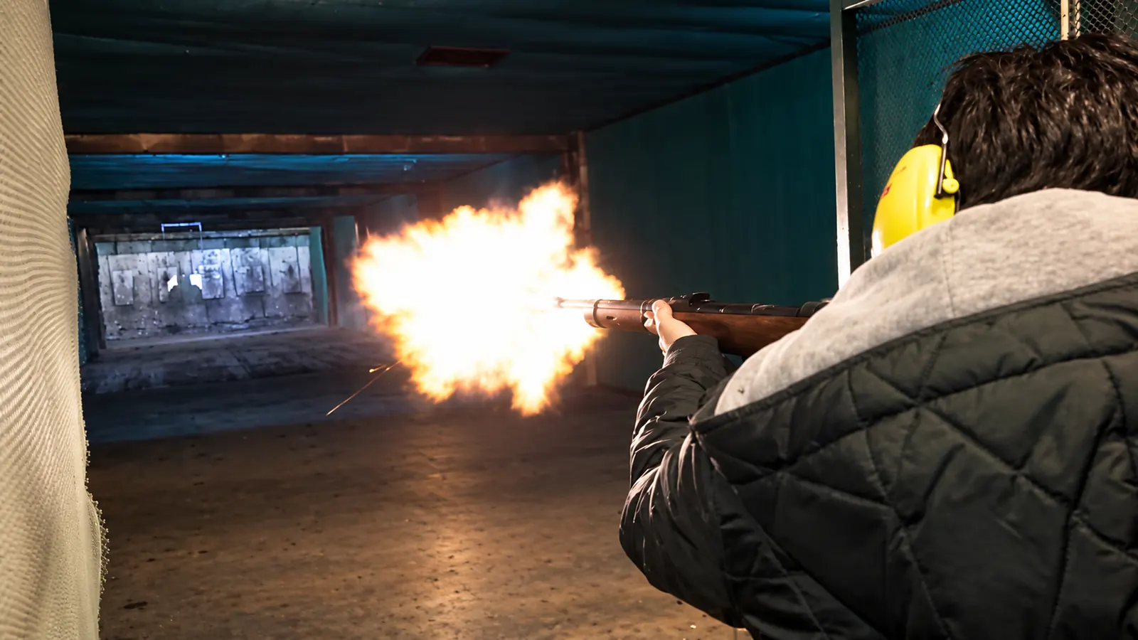 Rifle shooting with visible muzzle flash at a supervised indoor range