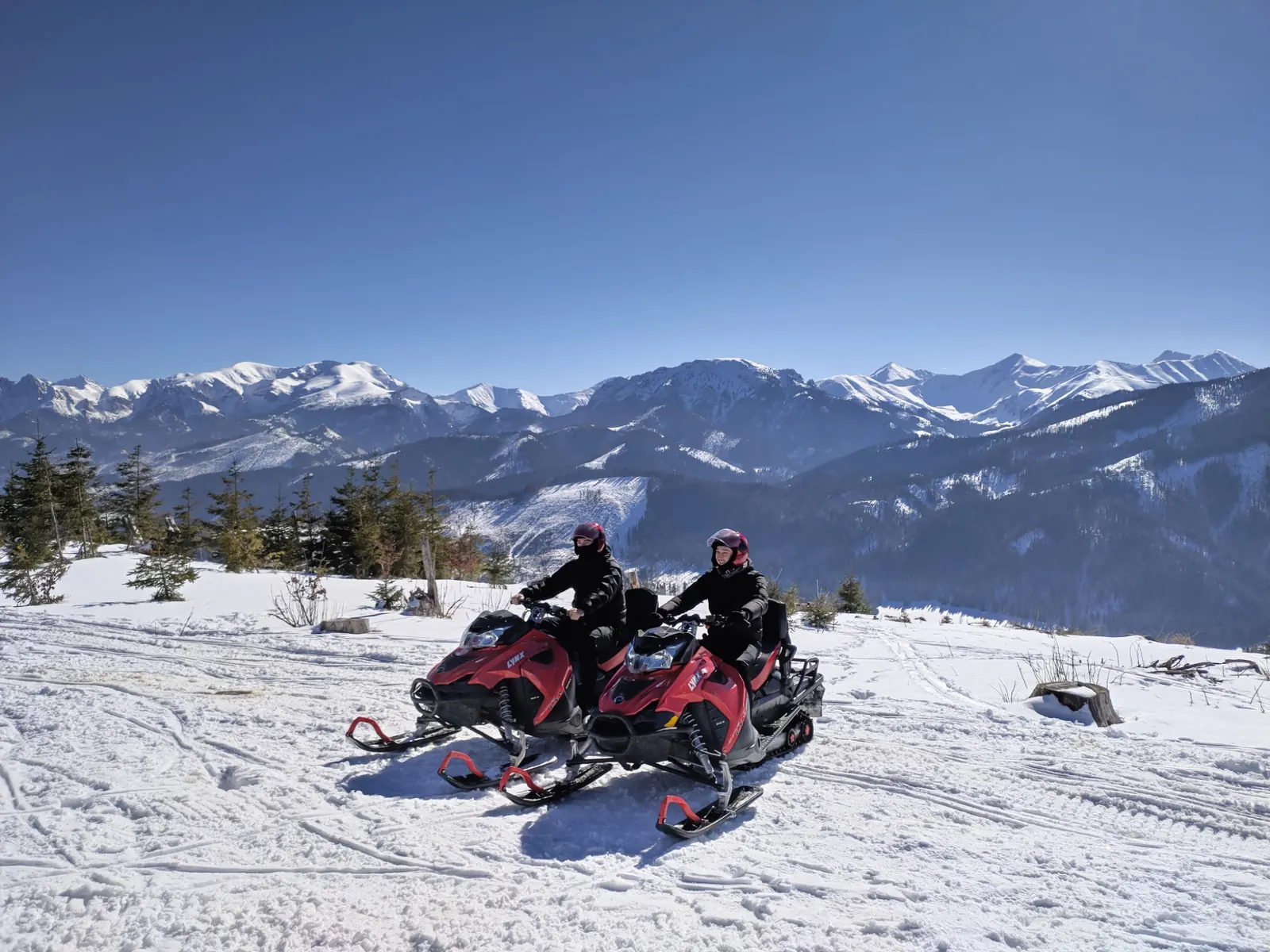 Two guests riding snowmobiles with the snowy Tatra Mountains behind them