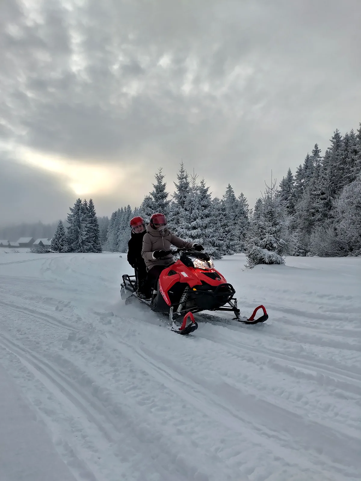 Two guests riding a snowmobile through a snowy Tatra forest