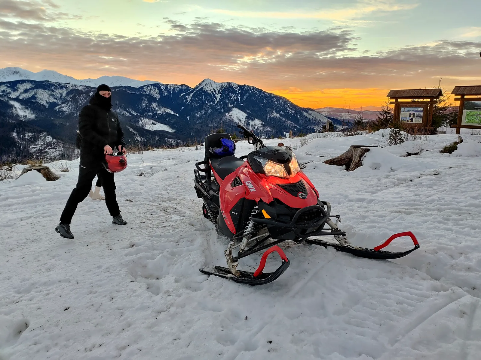 Red snowmobile overlooking the snowy Tatra Mountains at sunset